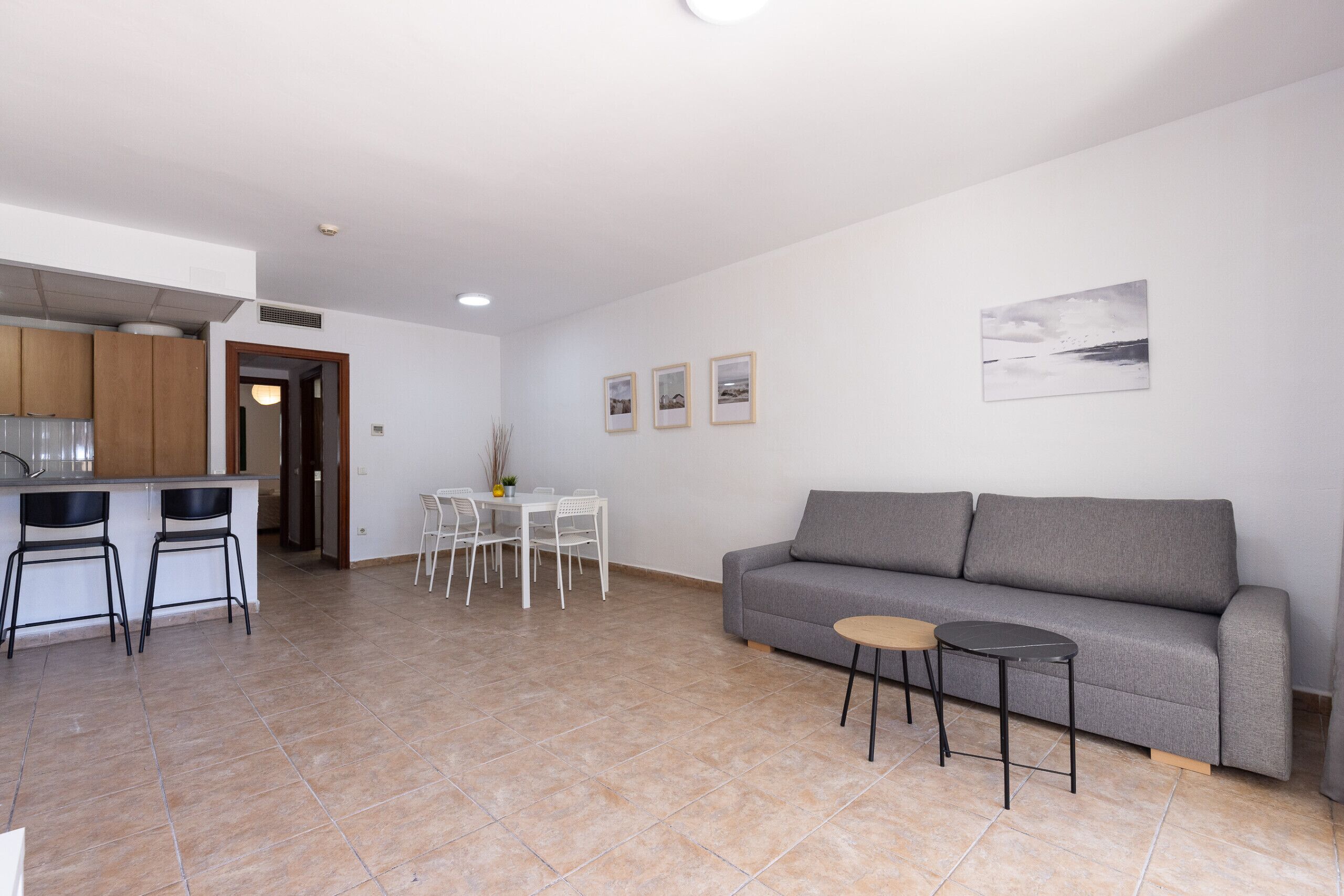 A modern living room with a grey sofa, a small round table, and a dining area with a white table and chairs.