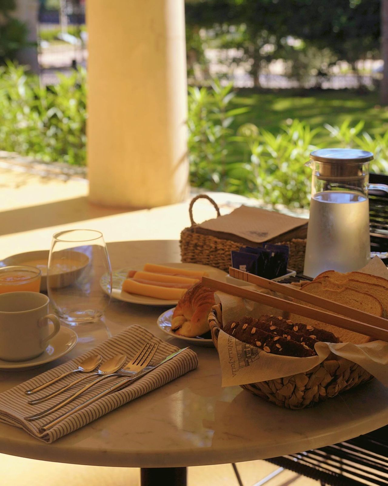 A breakfast table with a cup, glass, bread, croissant, and a thermos.