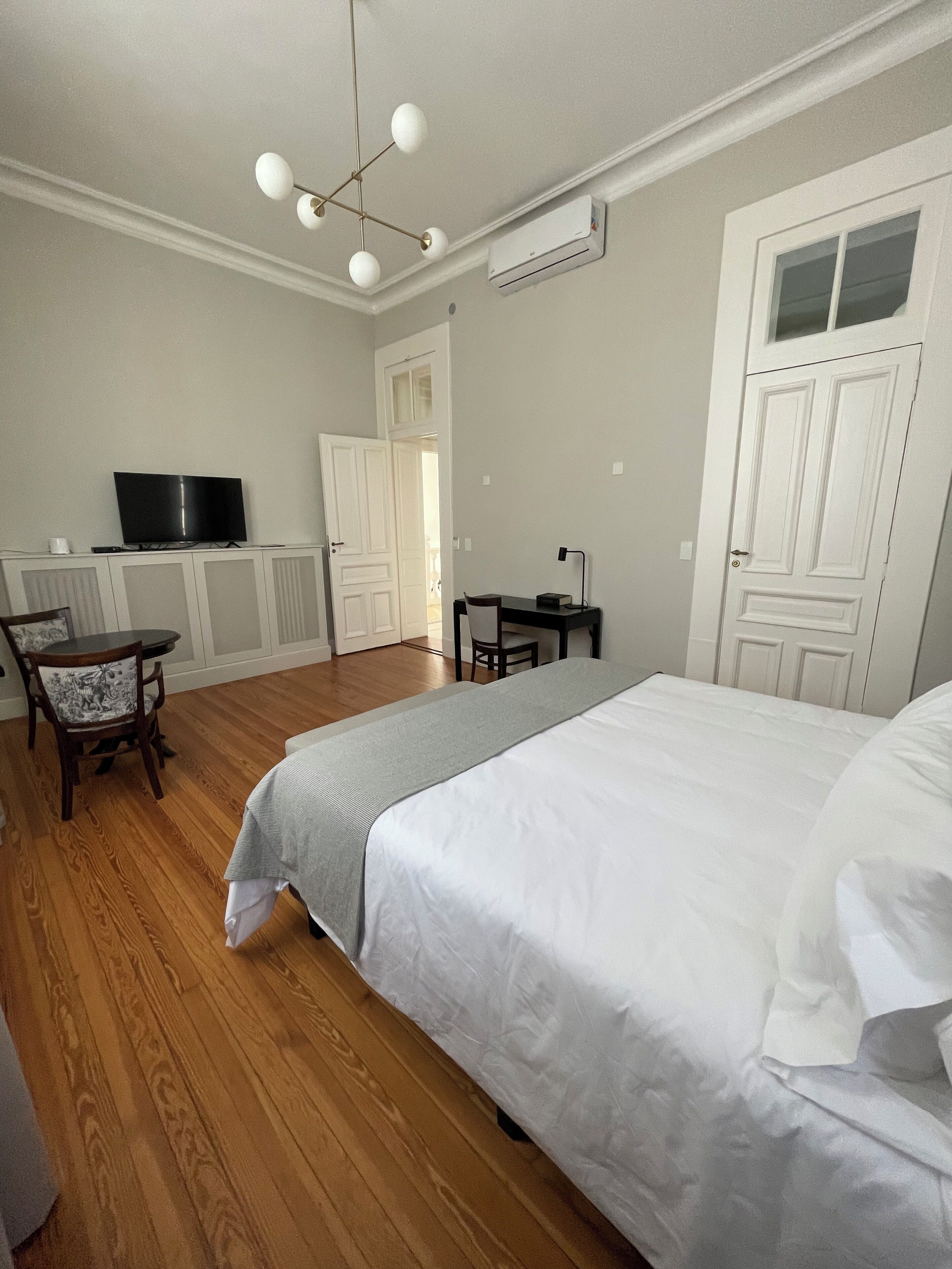 A bedroom with a bed, a desk, a chair, a television, and a door.