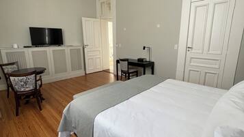 A bedroom with a bed, a desk, a chair, a television, and a door.