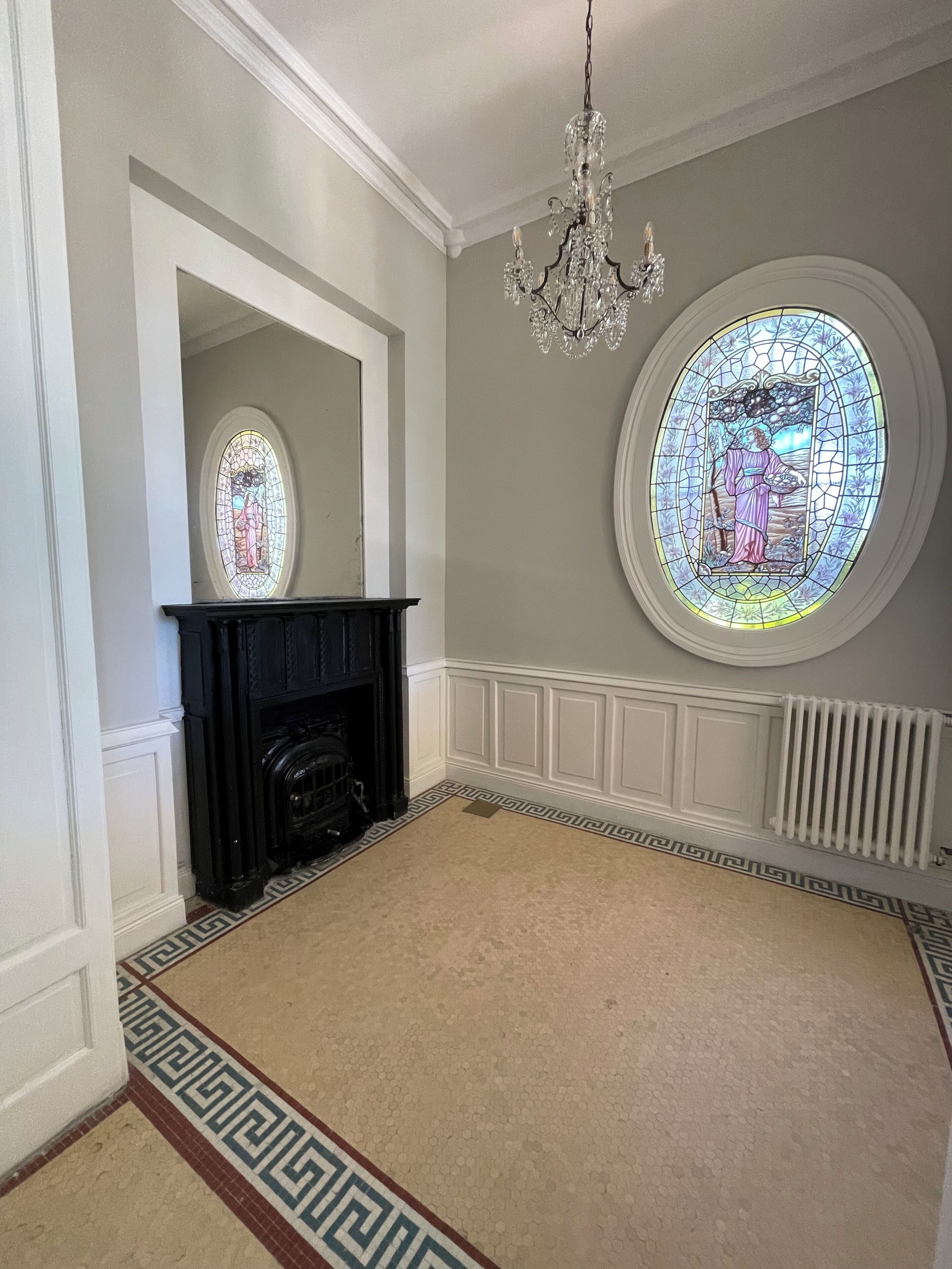 A room with a fireplace, a chandelier, and two stained glass windows.