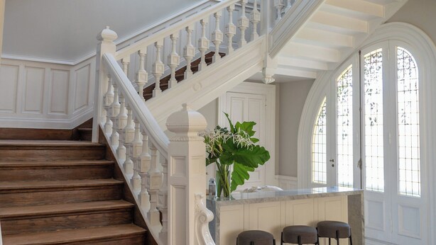 Una imponente escalera con barandillas blancas y escalones de madera que conduce a una zona de descanso con barra y taburetes.