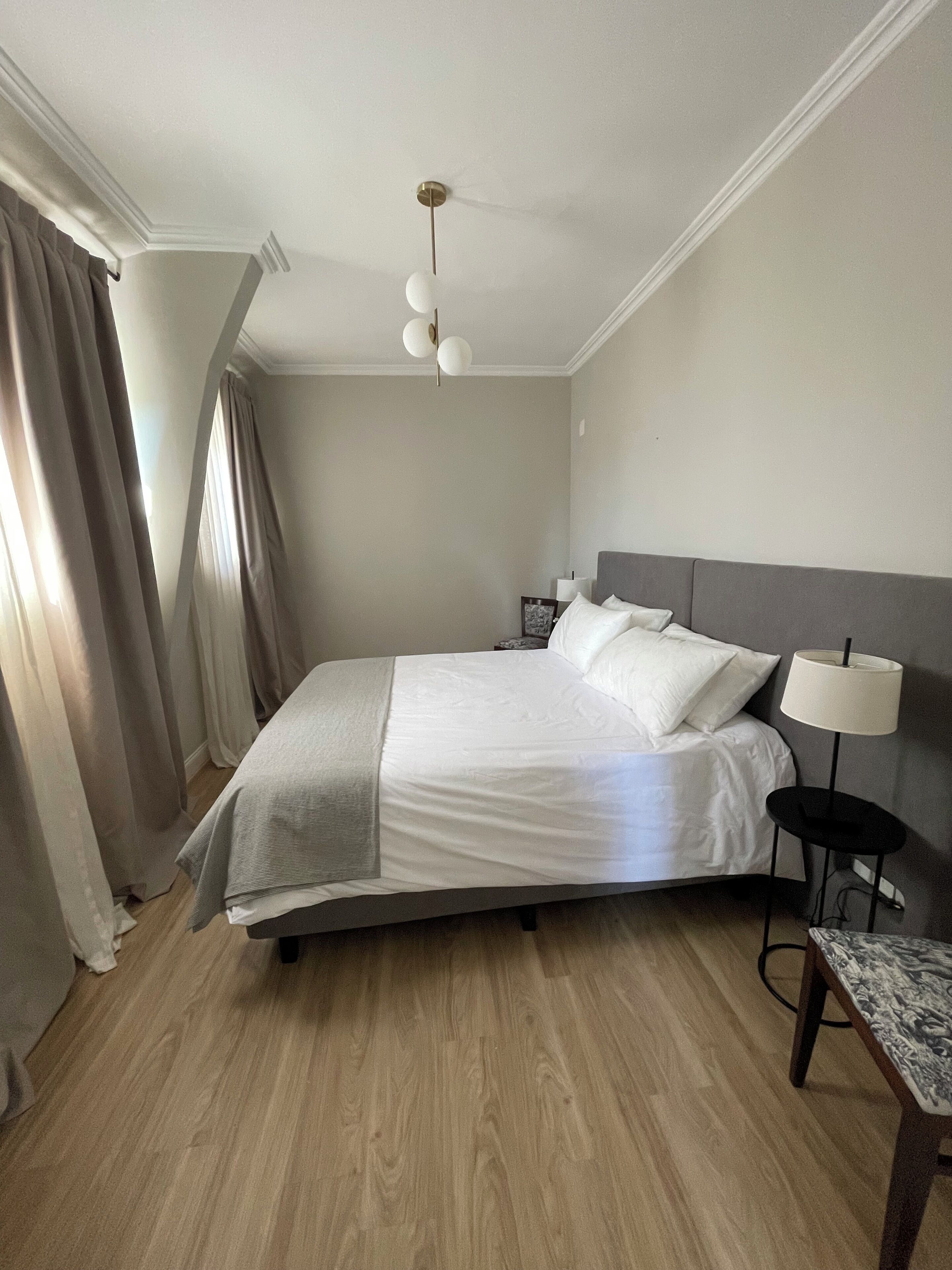 A neatly made bed with white linens, a grey headboard, and a bedside table with a lamp.