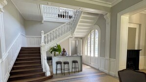 Amplia sala de estar con una imponente escalera, zona de bar con taburetes y un sillón grande.