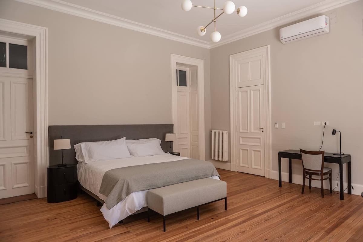 A bedroom with a bed, bedside tables, a desk, and an air conditioning unit.