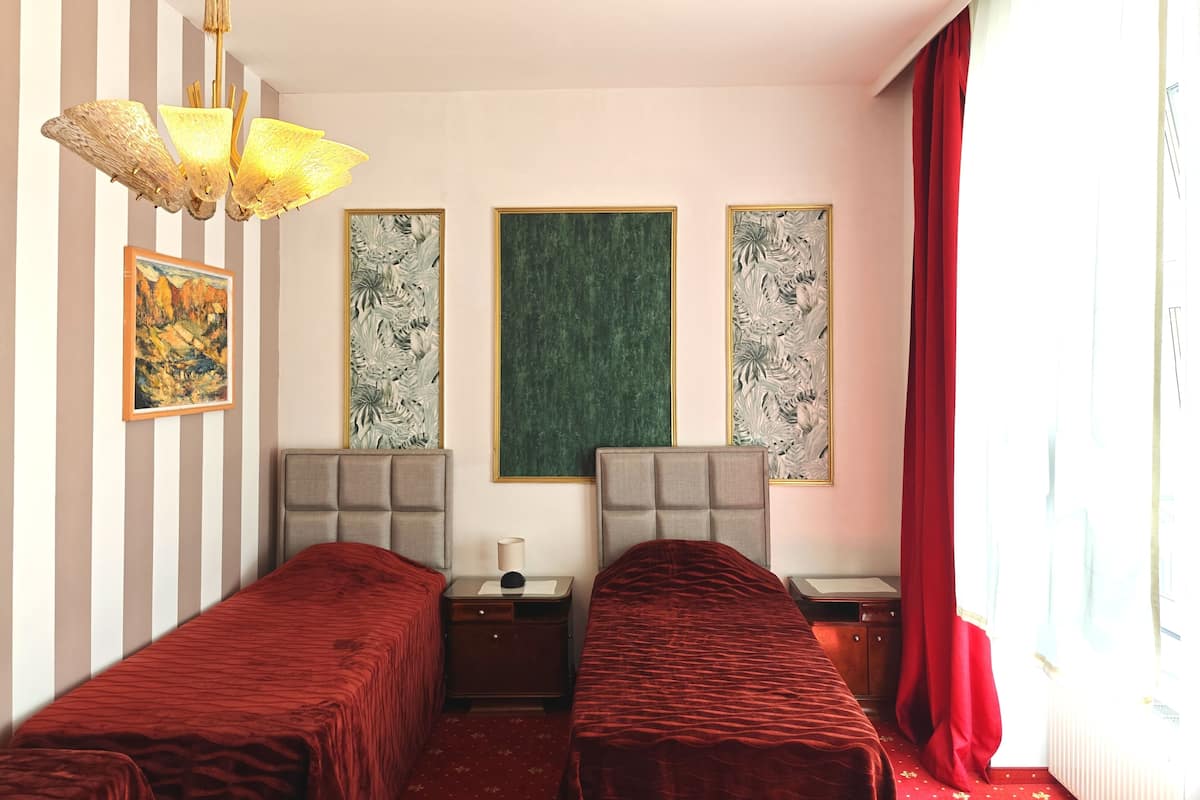 Ein Hotelzimmer mit zwei Betten, einer Kandelaber und drei gerahmten Kunstwerken an der Wand.