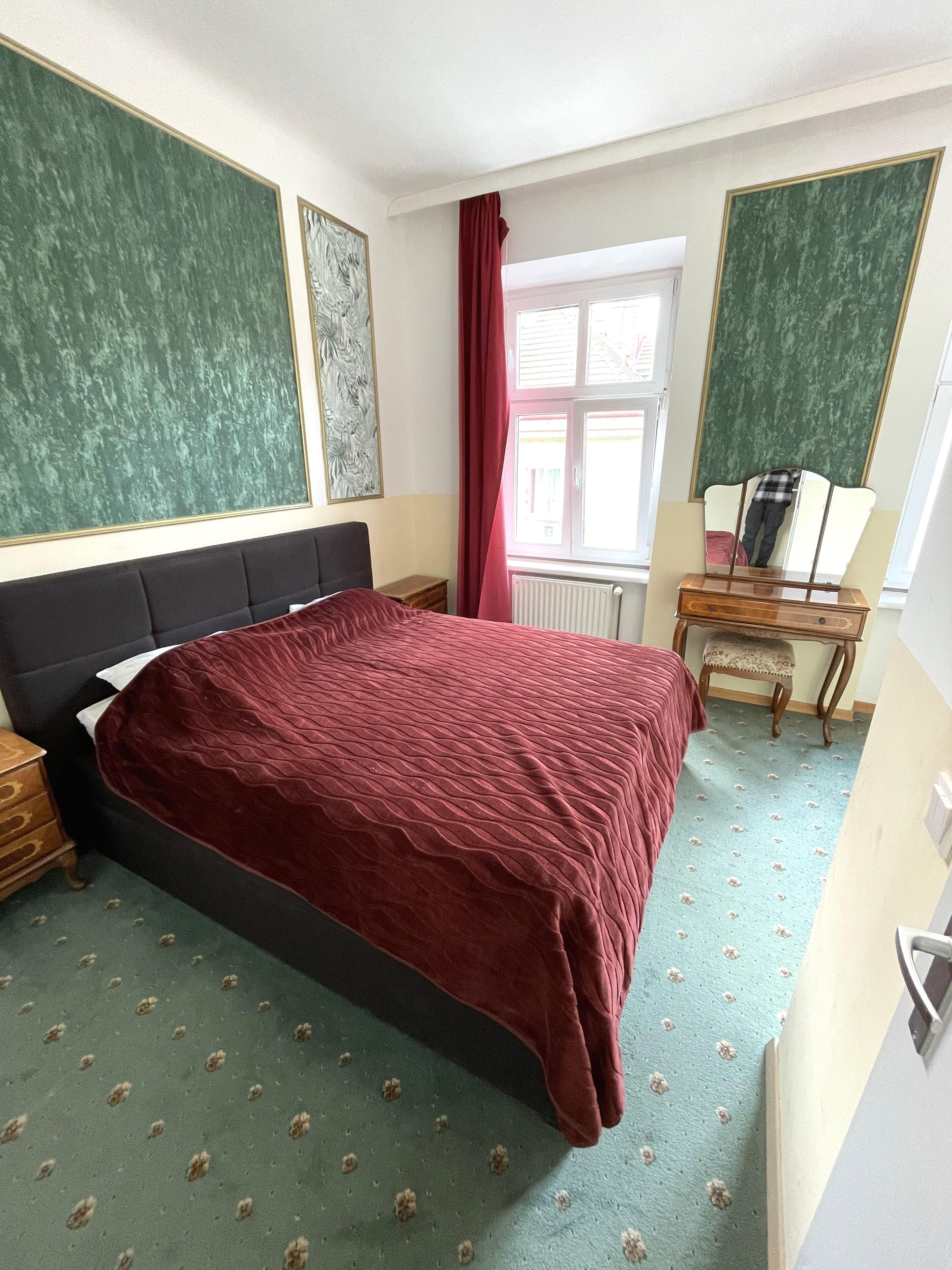 Un dormitorio con una cama grande, una mesita de noche de madera, un aparador y una ventana con cortinas.