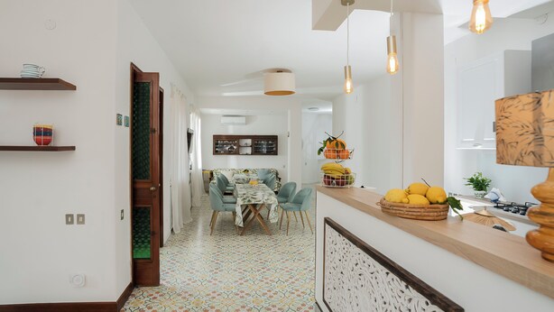 Une cuisine moderne avec un coin repas, agrémentée de luminaires suspendus, d’un sol à motifs et d’un panier de fruits.