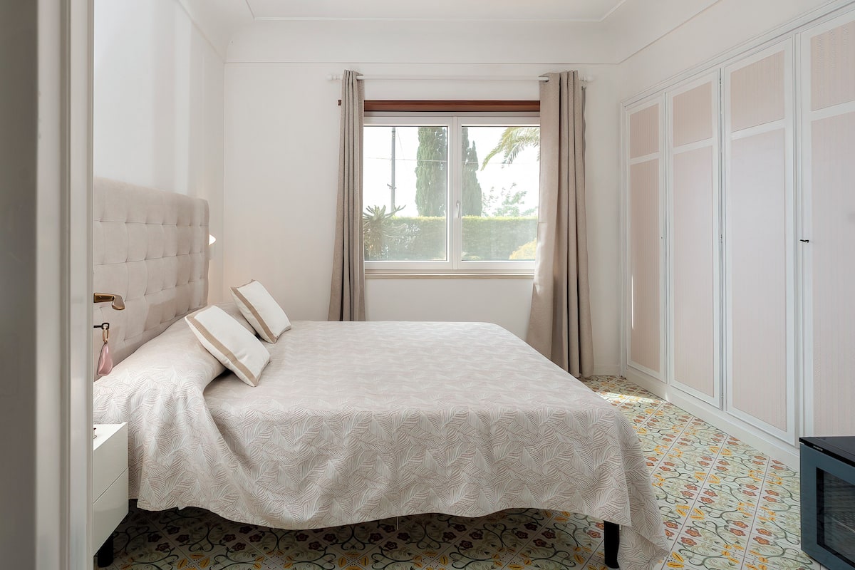 Un dormitorio con cama, ventana, armario y suelo estampado.