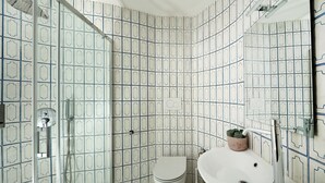 Une salle de bain équipée d’une douche, de toilettes et d’un lavabo, avec un carrelage au motif décoratif.