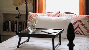 Ein ordentlich bezogenes Bett mit weißer Bettwäsche, ein Nachttisch mit Blumenvase und ein Bücherregal im Hintergrund.