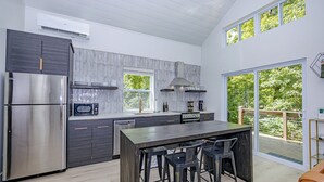 Cozinha moderna com geladeira de aço inoxidável, micro-ondas e fogão. Há uma janela grande com vista para o exterior.