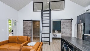 Um interior moderno com um quarto no mezanino, uma cozinha com frigorífico embutido e um sofá de couro.