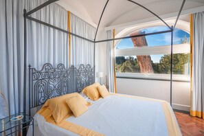 Un dormitorio con una cama grande, cortinas, una ventana que da a árboles y un cabecero de metal.