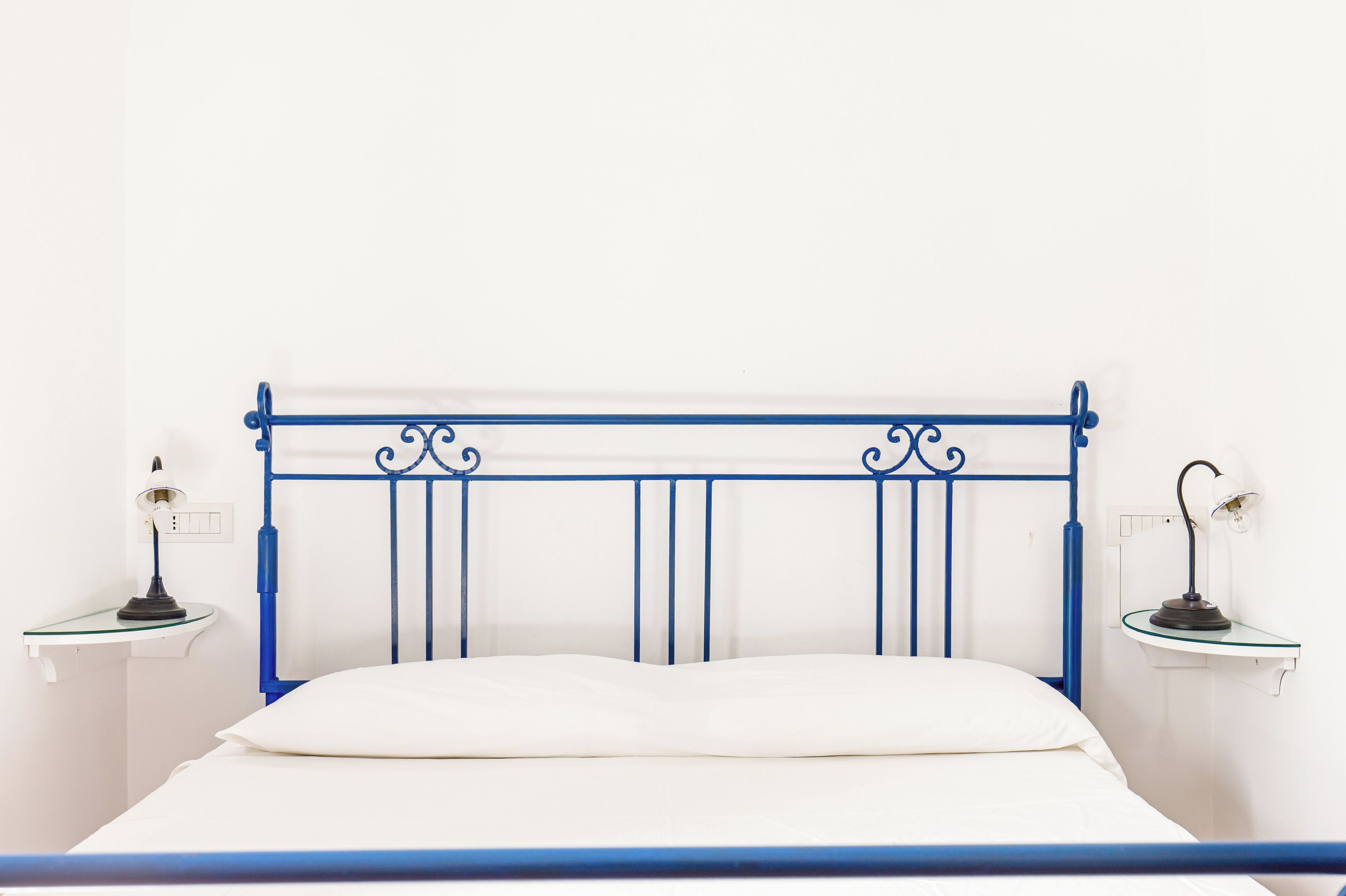 Ein Bett mit blauem Metall-Kopfteil, weißer Bettwäsche und zwei Nachttischen mit Lampen.