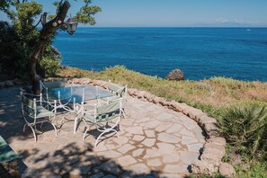 Un patio de piedra con mesa y sillas de vidrio con vistas al mar.