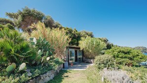 A secluded garden with a glass door entrance, surrounded by various plants and a stone wall. - Villa Serao & Cottage Camilla by MyVillaCollec... (Ischia Porto)