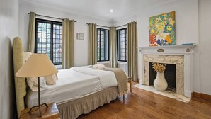 Une chambre d’hôtel avec un grand lit, une cheminée et deux fenêtres avec des rideaux.