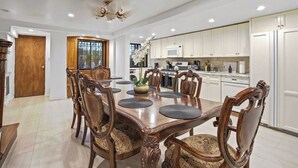 Un coin repas avec une table et des chaises en bois, un lustre et une cuisine dotée de meubles blancs.