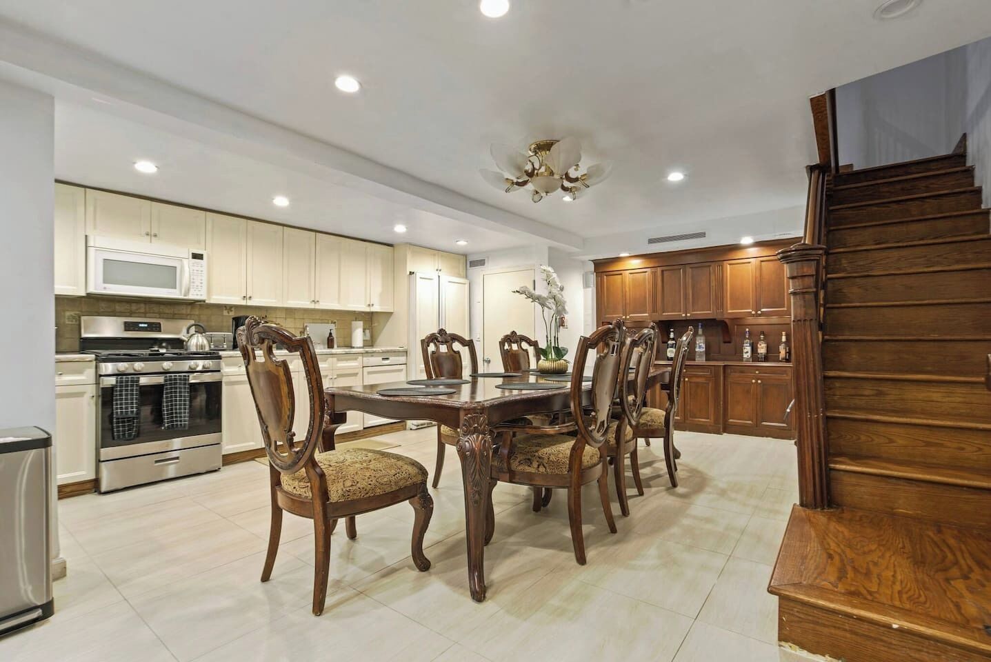 Una cocina moderna con armarios blancos, horno de acero inoxidable y comedor con mesa y sillas de madera.