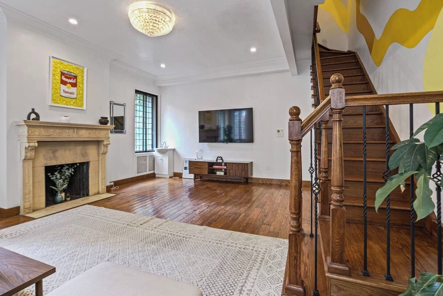 A spacious living room with hardwood flooring, a fireplace, a large TV, and a staircase with wooden railings.