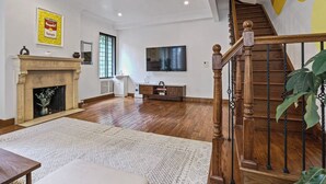 Un salon spacieux doté d’un parquet, d’une cheminée, d’un grand téléviseur et d’un escalier avec des rampes en bois.