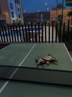 A tennis court with two paddles and a ball, surrounded by a fence and buildings in the background. - Apartamento Conjunto Residencial en Cartago Valle (Cartago)