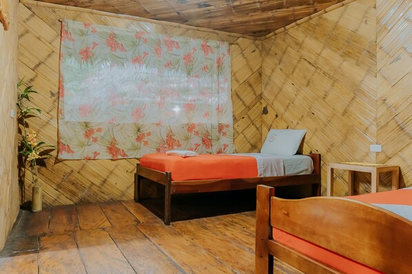 A room with a wooden floor, a bed with an orange bedspread, a wooden headboard, a nightstand, and a large floral curtain. - Piranha Eco-Lodge with Guided Tour (Cuyabeno)