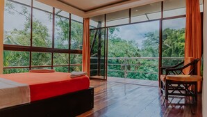 A spacious bedroom with a large bed, a wooden floor, and a view of lush greenery through large windows. - Piranha Eco-Lodge with Guided Tour (Cuyabeno)