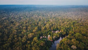 An aerial view of a forested area with a small cluster of buildings near a river. - Piranha Eco-Lodge with Guided Tour (Cuyabeno)