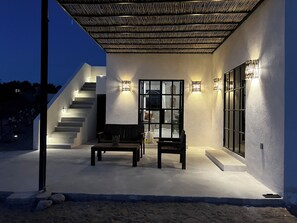 Une terrasse extérieure moderne, dotée d’un escalier menant à un espace abrité, d’un coin salon et d’une grande fenêtre.