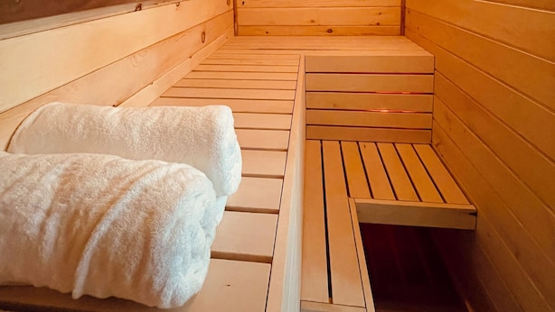 A wooden sauna with benches and benches, a bench with towels, and a light fixture on the ceiling. - Peaceful space in the country. Deck&private indoor sauna. Surrounded by nature! (Horseheads)