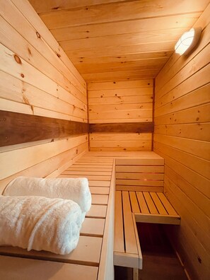 Un sauna en bois avec des bancs, un banc avec des serviettes et un luminaire au plafond.