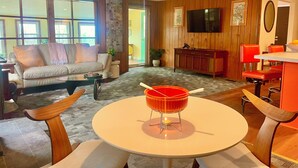 A modern living room with a sofa, a coffee table, and a TV mounted on the wall. - Peaceful space in the country. Deck&private indoor sauna. Surrounded by nature! (Horseheads)