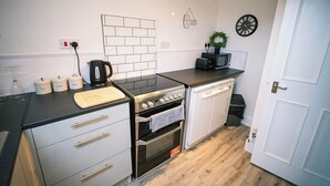 Eine moderne Küche mit Gaskochfeld, Backofen und Mikrowelle. Es gibt Schränke, eine Arbeitsplatte und eine Tür mit Griff.