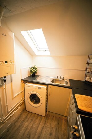 A compact kitchen with a built-in washing machine, a sink, and a small window above the countertop.
