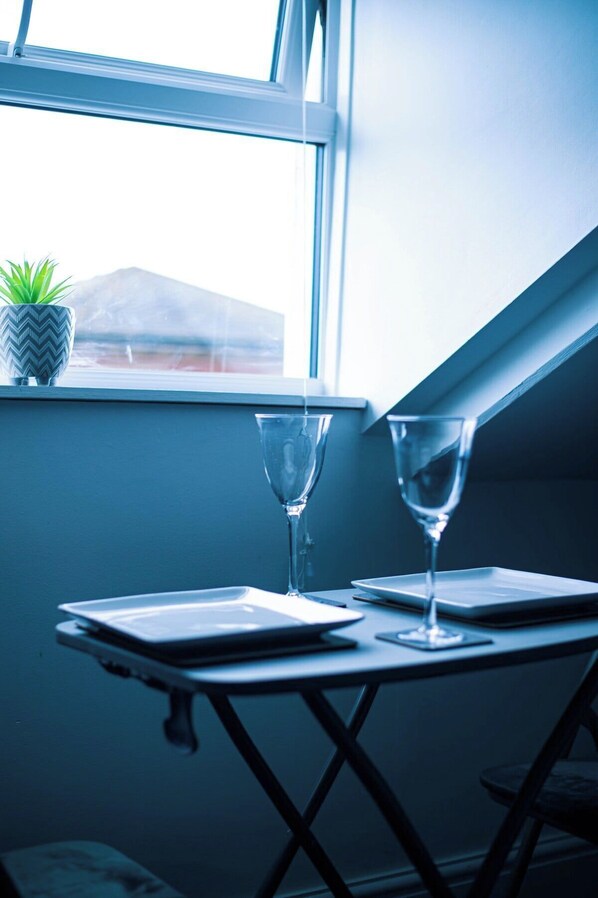 A table with two wine glasses and a plate, positioned near a window with a view of a mountain.