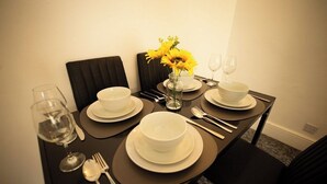 A dining table set with white plates, bowls, cutlery, and wine glasses, with a vase of yellow flowers in the center. - 20%OFF|MonthlyEscape|Family|Leisure|WiFi|Sleeps4 (Suffolk)