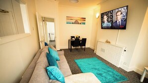 A living room with a sofa, a dining table, and a TV mounted on the wall. - 20%OFF|MonthlyEscape|Family|Leisure|WiFi|Sleeps4 (Suffolk)