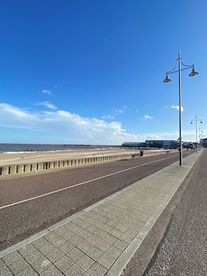 A coastal promenade with a paved walkway, benches, and street lamps.