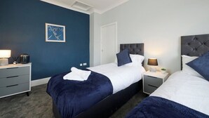 A hotel room with two beds, a dark blue accent wall, and a framed artwork.