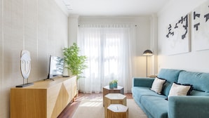 Ein modernes Wohnzimmer mit einem Holzkonsolentisch, einem blauen Sofa und einem großen Fenster mit transparenten Vorhängen.