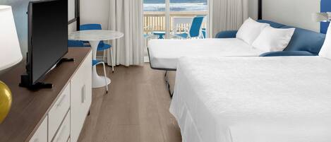 Une chambre d’hôtel avec deux lits, une télévision, un bureau et vue sur la plage.