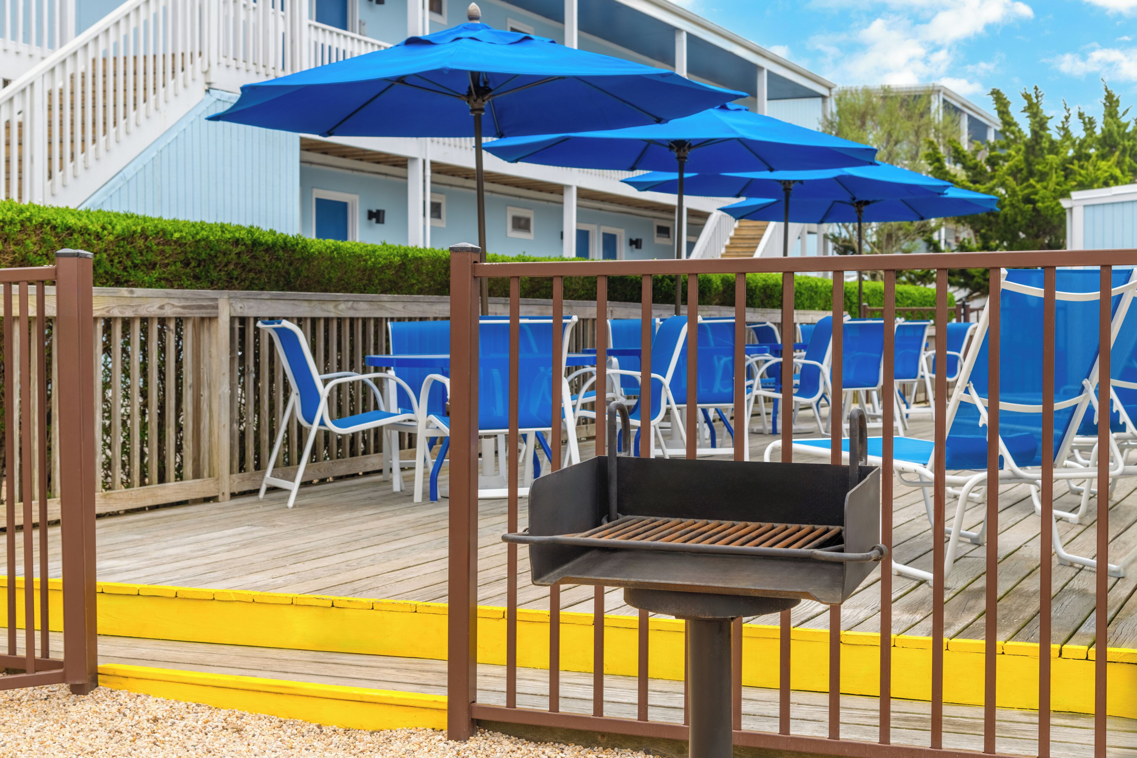 A pool area with blue umbrellas, lounge chairs, and a barbecue grill.