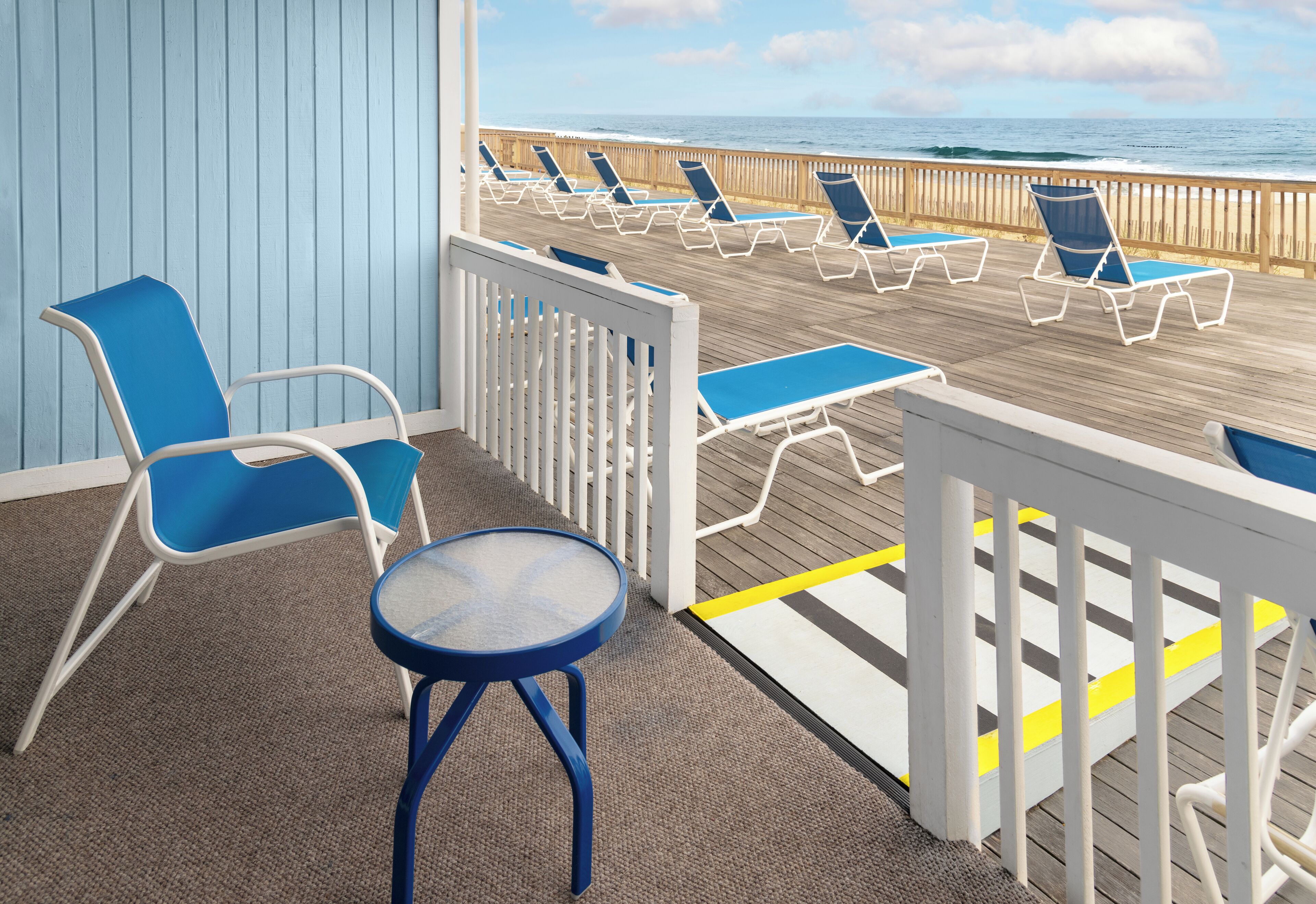 Une terrasse avec des chaises longues bleues et une table, offrant une vue sur l’océan.