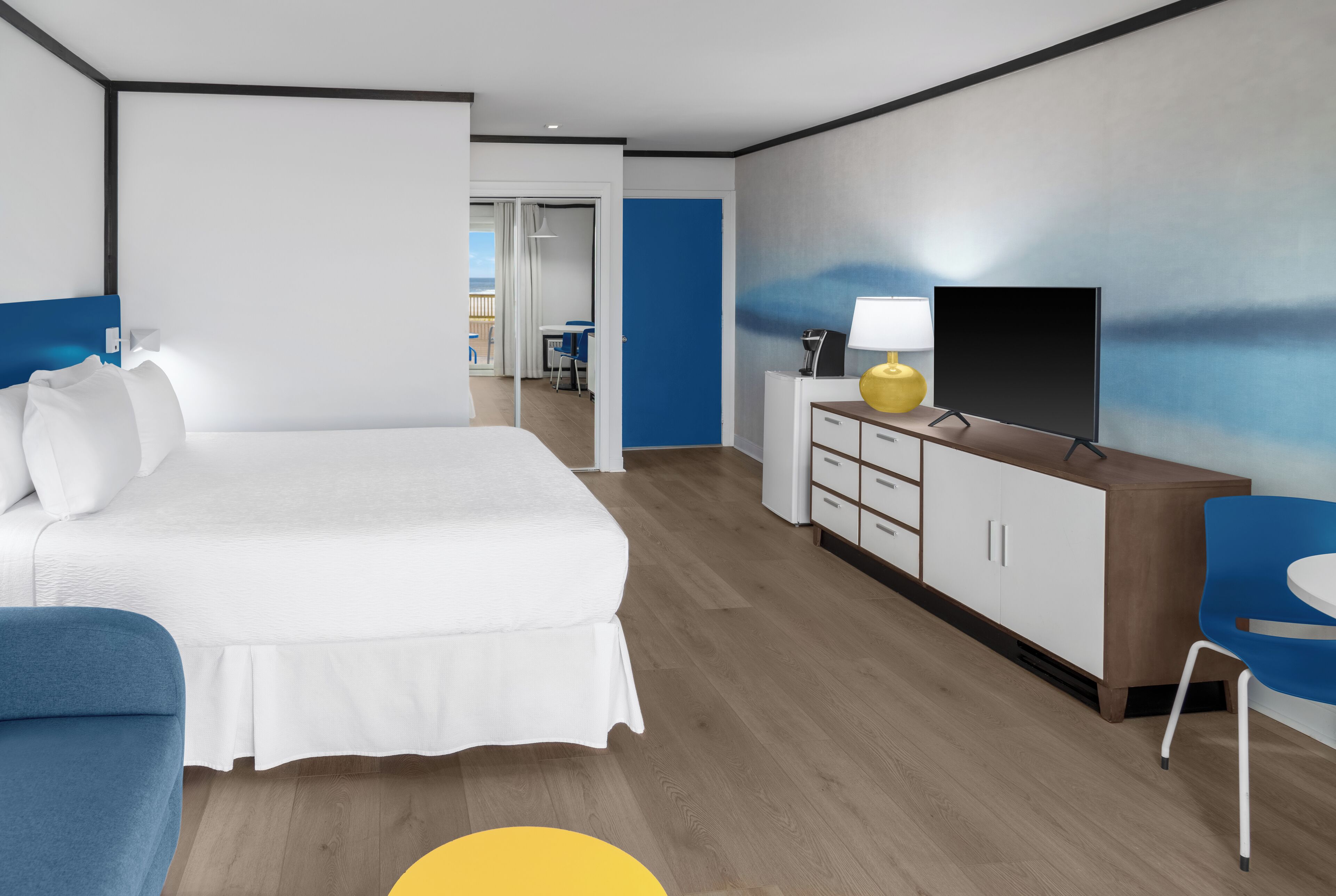 A modern hotel room with a large bed, a desk with a TV, and a view of the balcony.