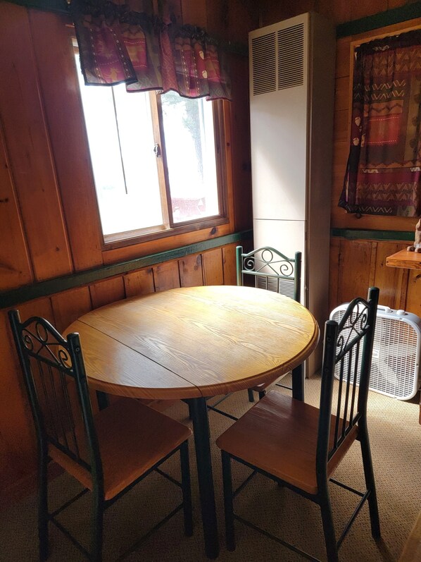 Una mesa de comedor de madera con cuatro sillas, una ventana con cortinas y un equipo de aire acondicionado blanco.
