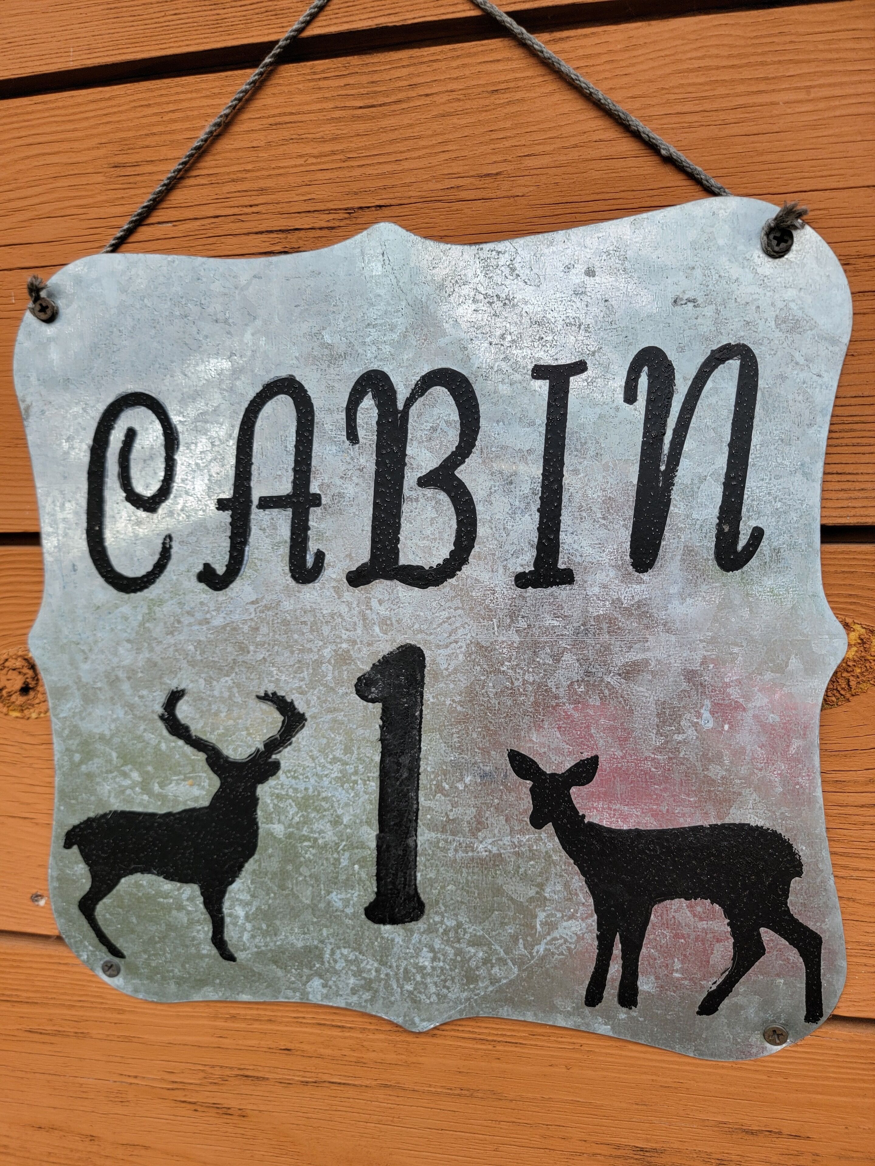 A metal sign with the text "CABIN 1" and silhouettes of two deer.