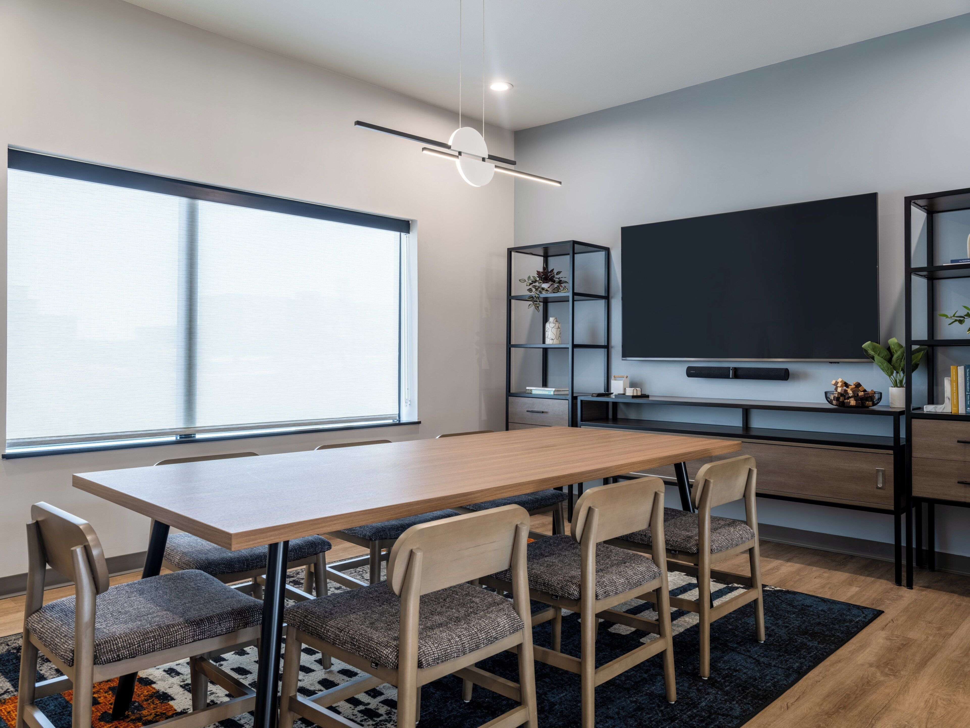Een moderne woonkamer met een houten eettafel, vier stoelen, een televisie en een boekenkast.