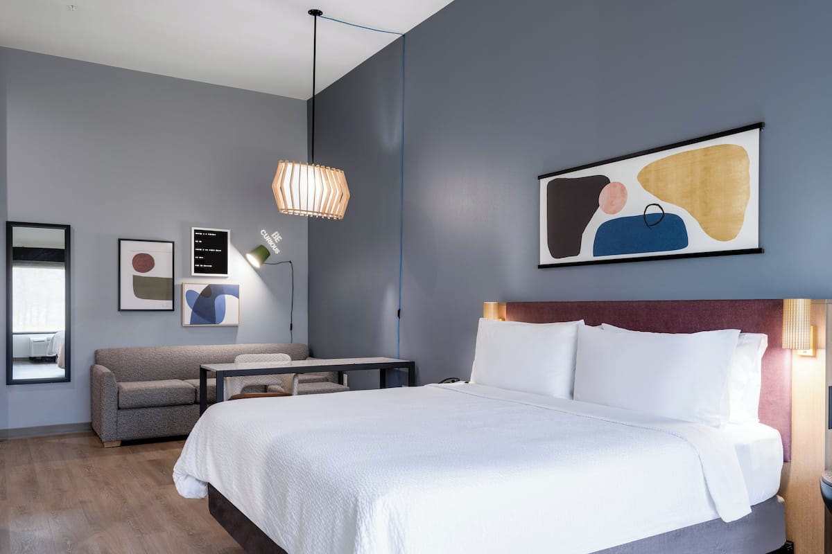 A modern hotel room with a large bed, a seating area with a table, and artwork on the walls.